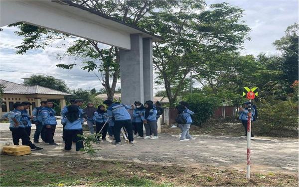 Mahasiswa berlatih pengukuran di lingkungan kampus dengan rambu ukur di kejauhan